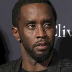 Sean Combs wearing a dark jacket, black t-shirt and silver chains on his neck