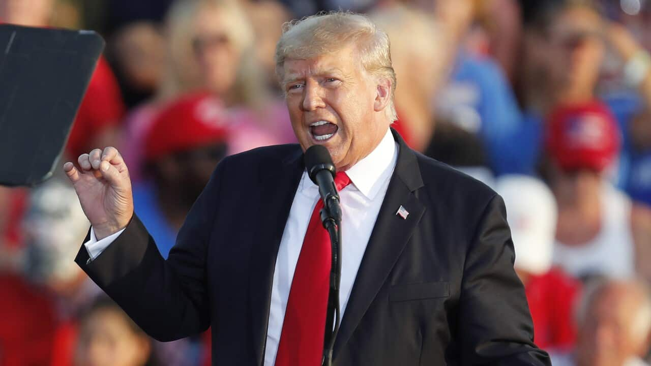 Donald Trump, wearing a black suit and a red tie, addresses a rally.