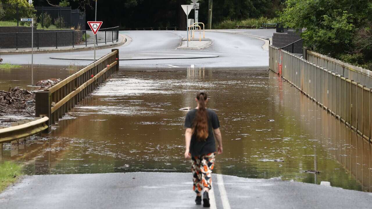 A woman facing away from the camera looking at floodwater over a bridge.