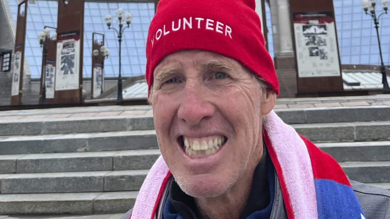 A man in a red beanie and a colourful muffler is grinning.