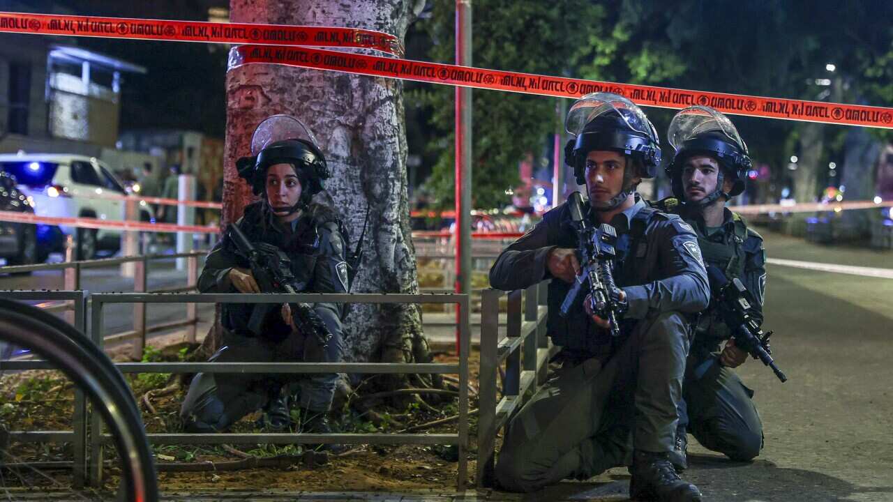 Three Israeli police wearing helmets and carrying machine guns kneeling next to a tree