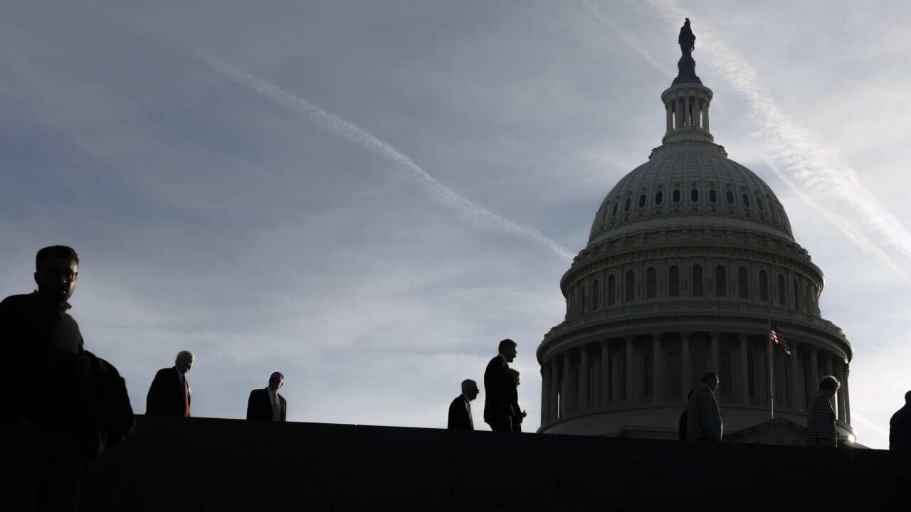 Silhouettes of people walking past the Capitol building in Washington, DC.