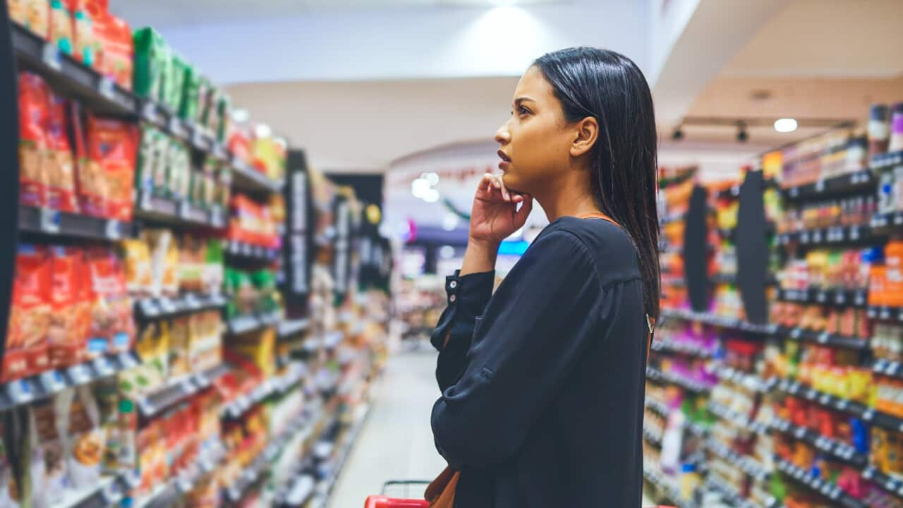 A young woman looks at items in a supermarket aisle.