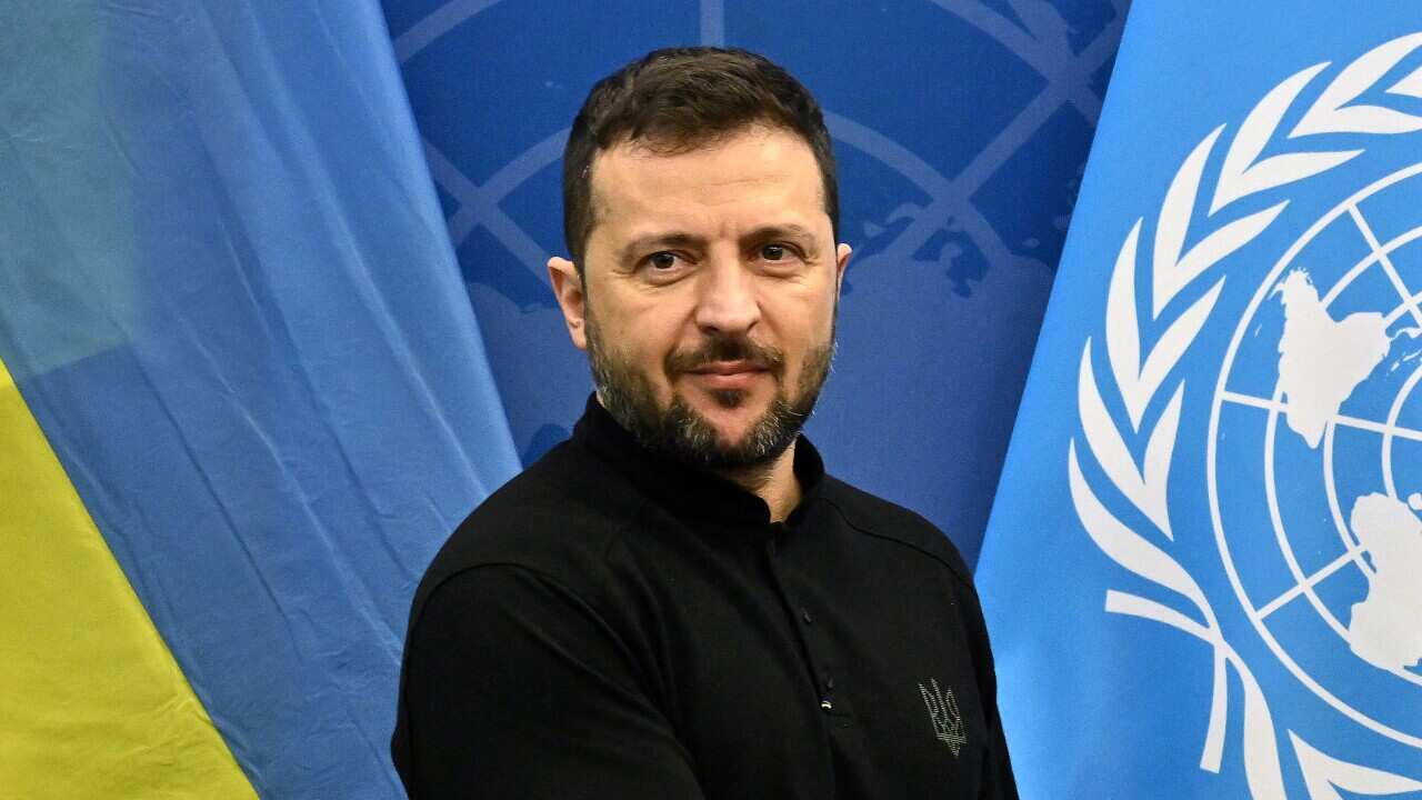 Volodymyr Zelenskyy poses for a photo with UN flags in the background.