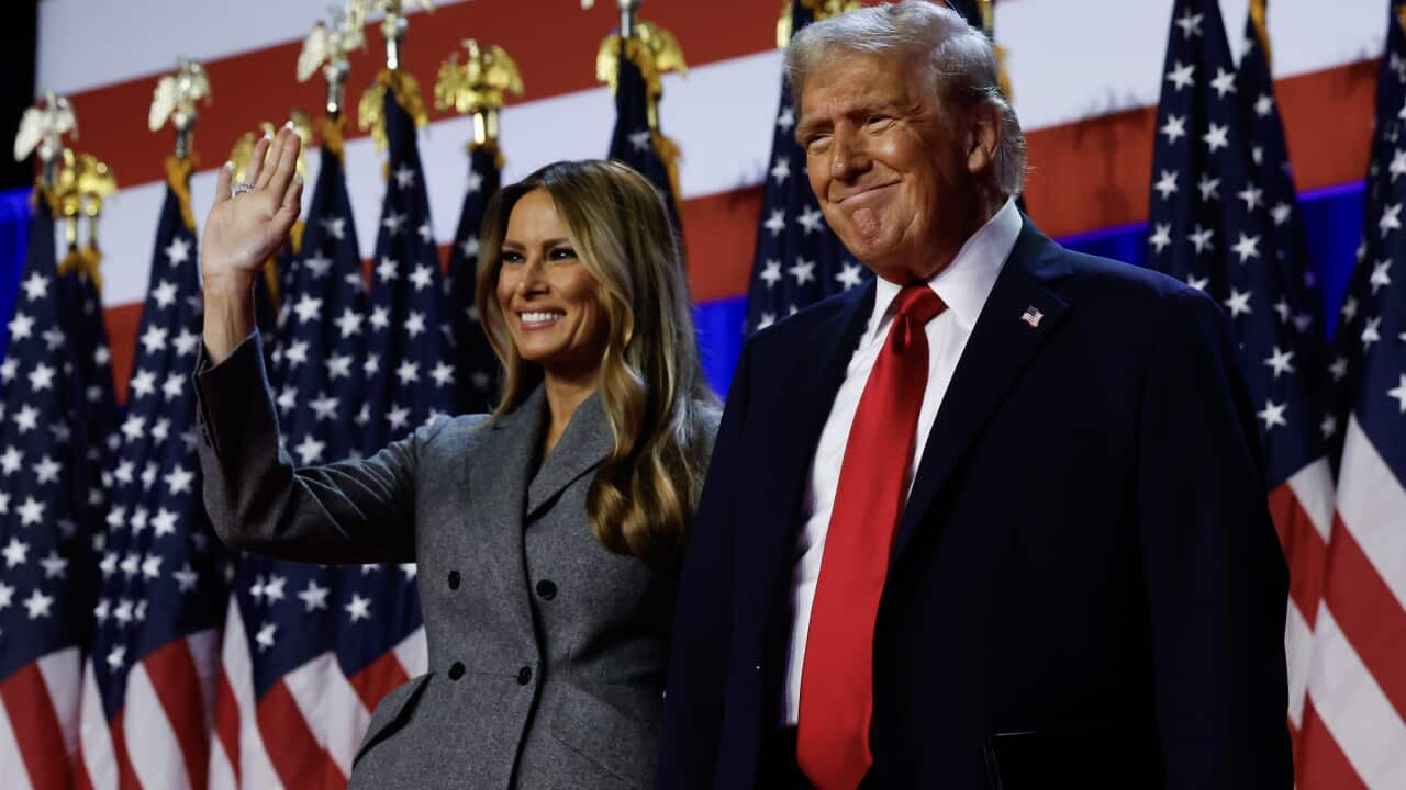 Donald Trump and his wife Melania wave as they smile while standing on stage.