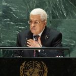 A man speaking at a podium, with green tile behind him. The United Nations logo is on the front of the podium.