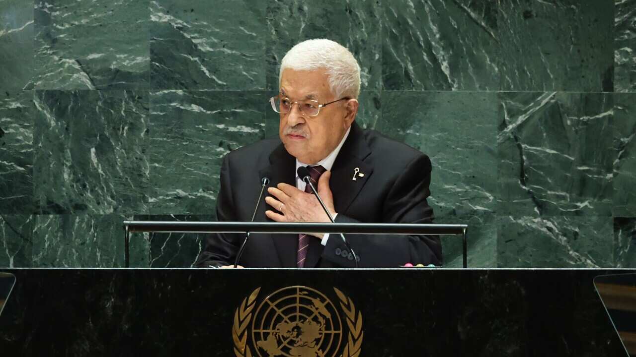 A man speaking at a podium, with green tile behind him. The United Nations logo is on the front of the podium.